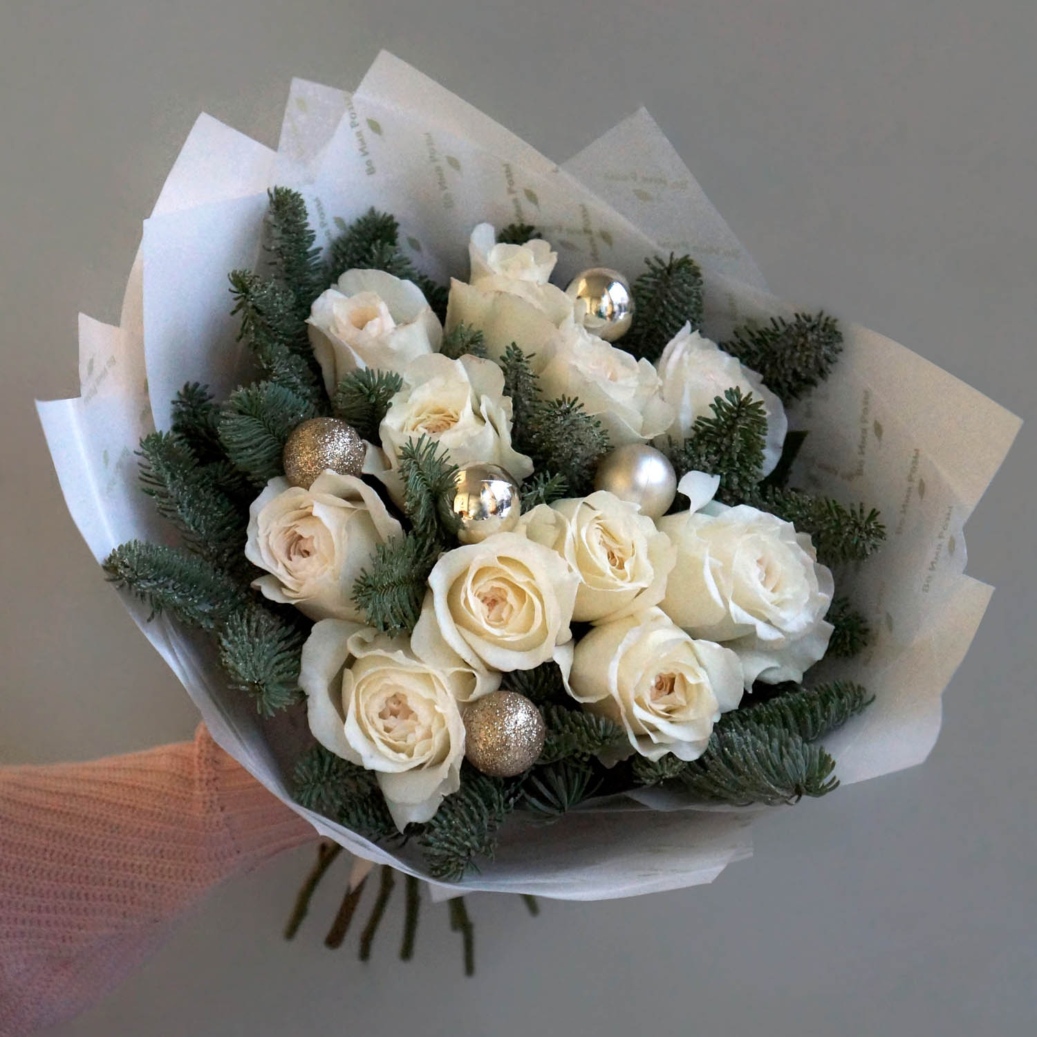 новогодний букет с нобилисом и белыми розами в фирменной бумаге во имя розы и новогодним декором