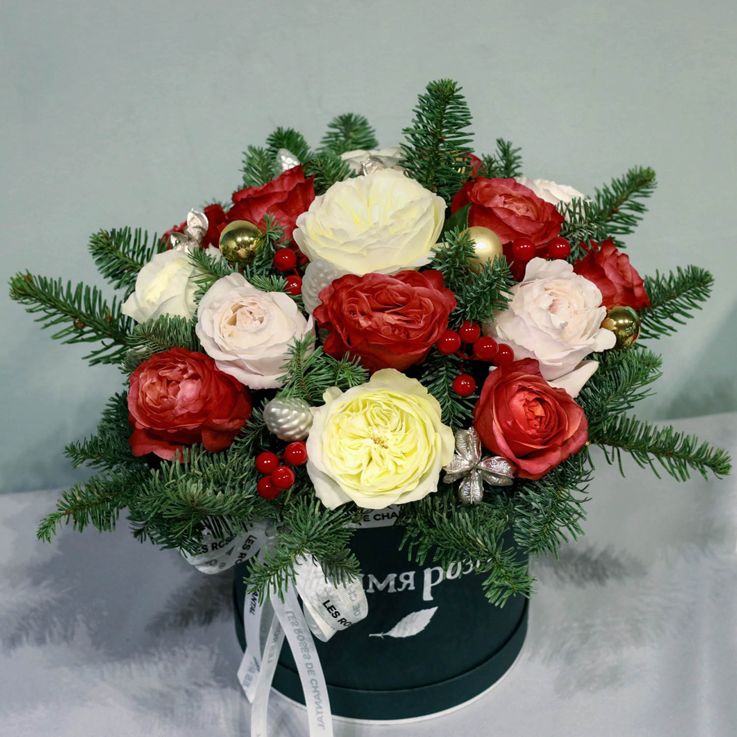 новогодняя композиция в шляпной коробке с алыми и персиковыми розами, нобилисом и декором